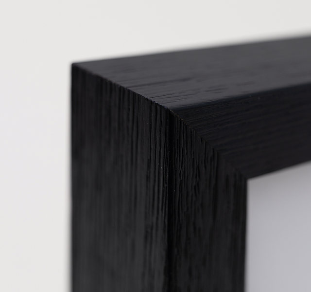 Close-up of the corner of a black wooden photo frame with a white print inside, against a light gray wall