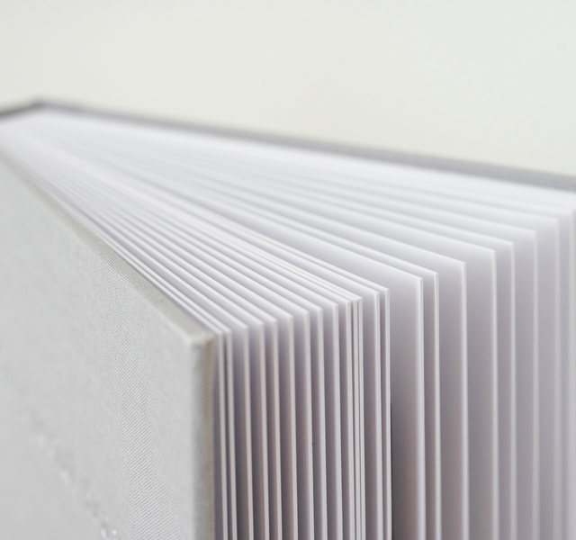 Close-up of the thick white pages of a lay-flat photobook, stacked edge to edge against a soft gray background