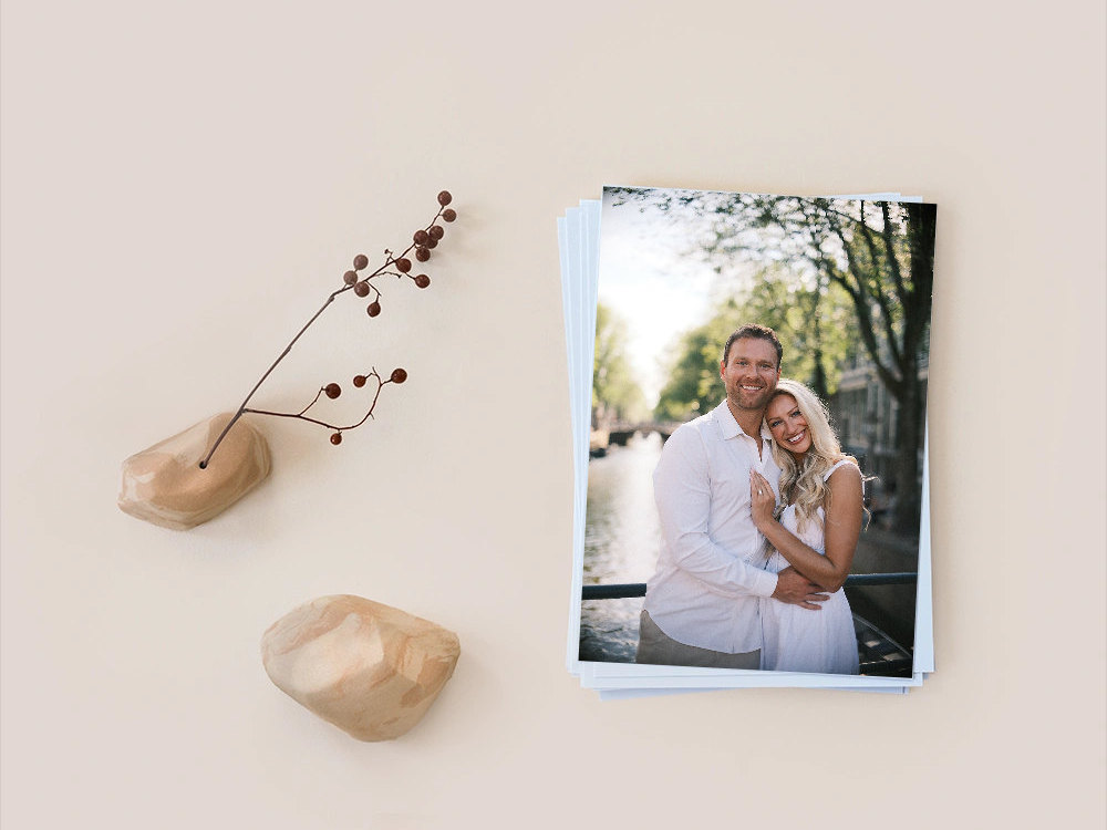 Stack of prints with a couple embracing by an Amsterdam canal on top, beside two smooth stones and a dried branch with red berries