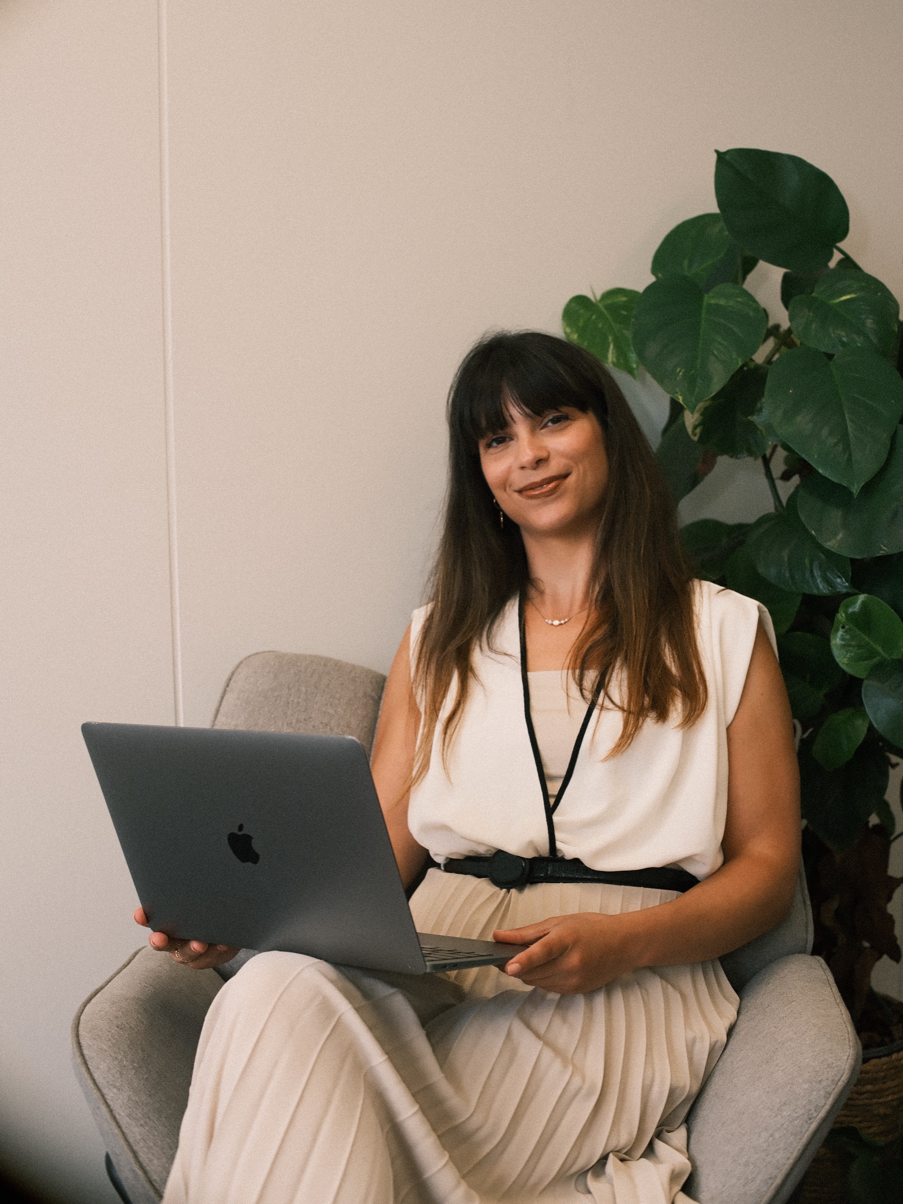 Smiling woman with a lanyard and a laptop on her lap in a gray armchair, the last portrait of the branding shoot