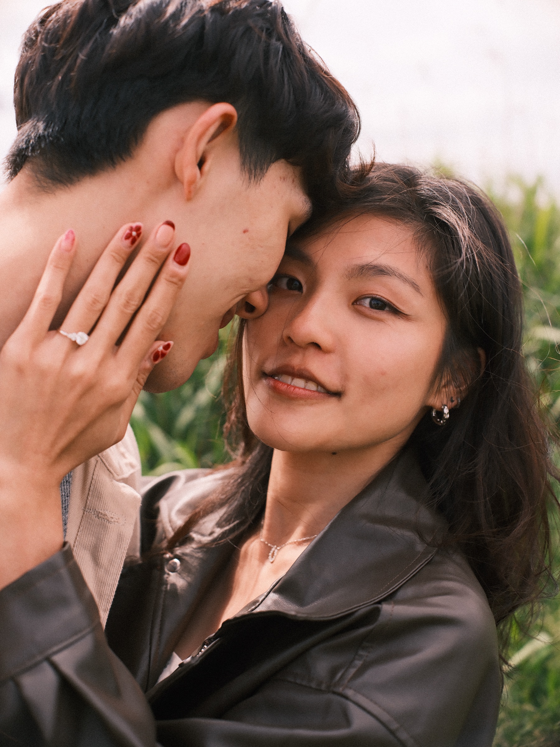 Close portrait of her looking into the lens, her ring hand with red nails resting on his cheek as they lean their heads together