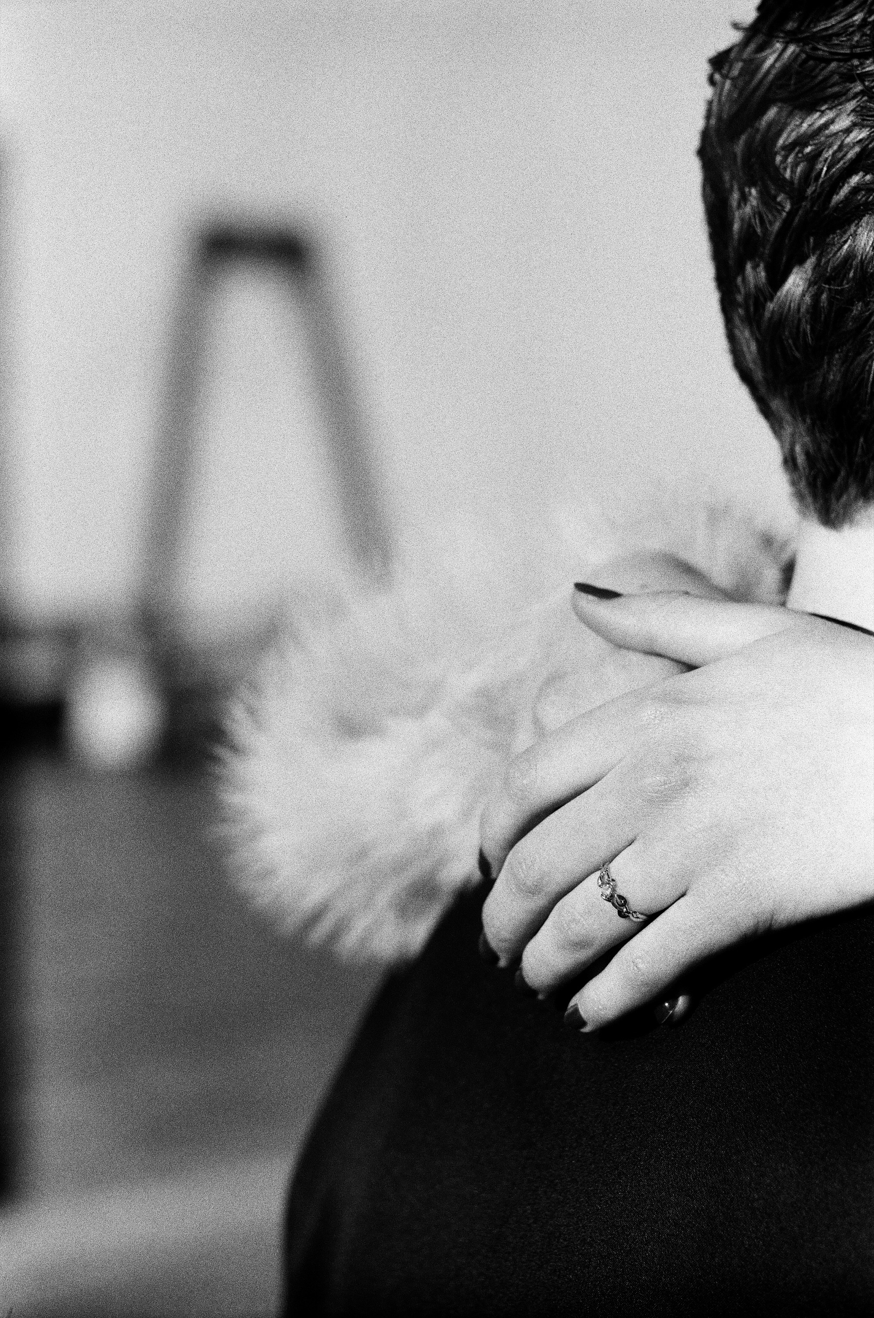Ring on her hand as it rests on the shoulder of his black jacket, the Willemsbrug blurred far behind, a detail from their proposal in Rotterdam