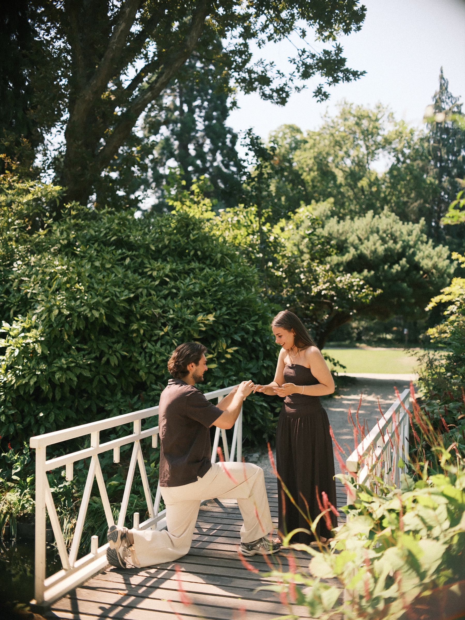 Kneeling on the planks, he slides the ring onto her finger while she looks down at it, framed by the white railings