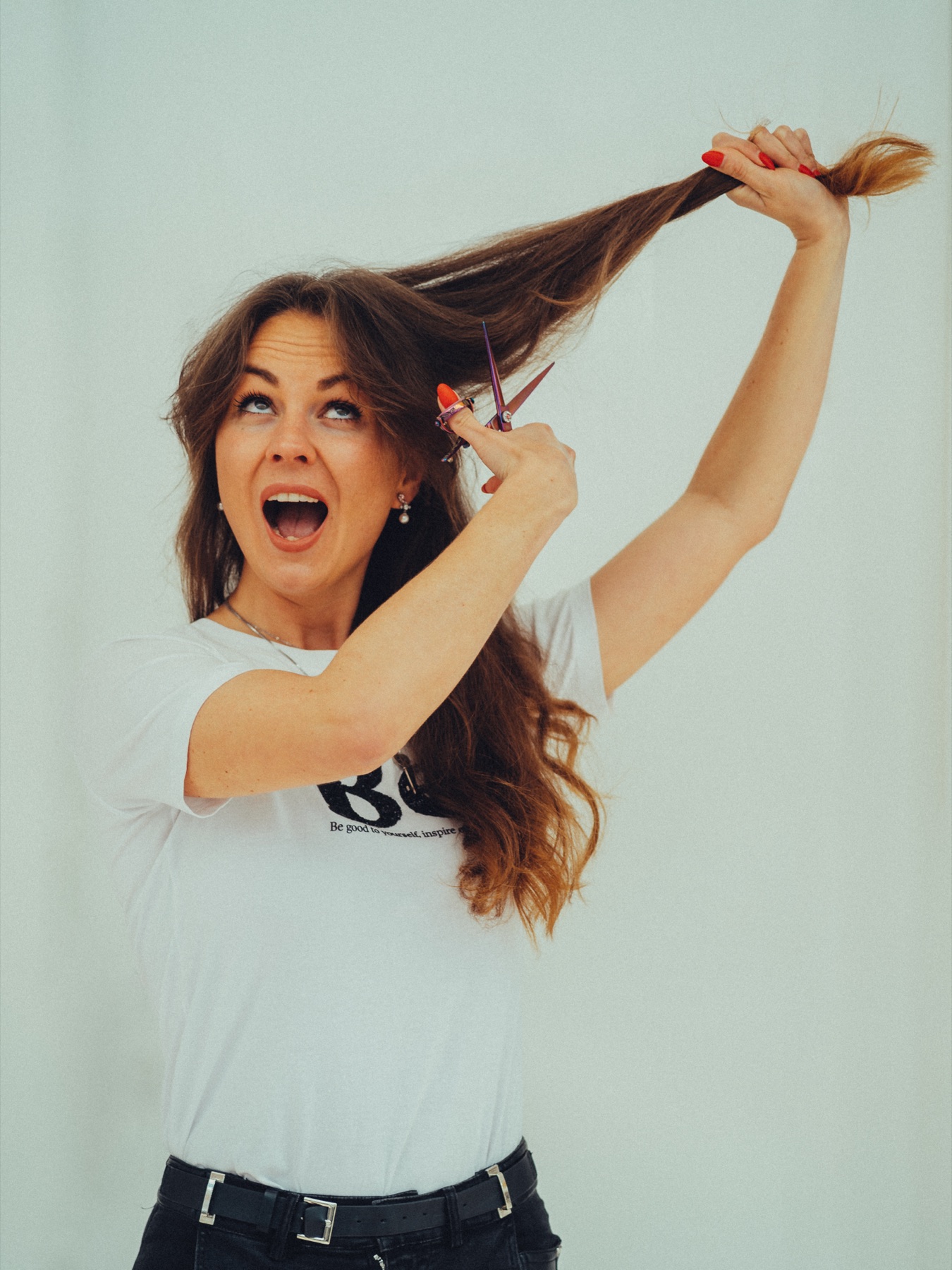 Eigenaar in een Be-shirt doet alsof ze haar eigen lange haar knipt, met open mond van gespeelde verbazing