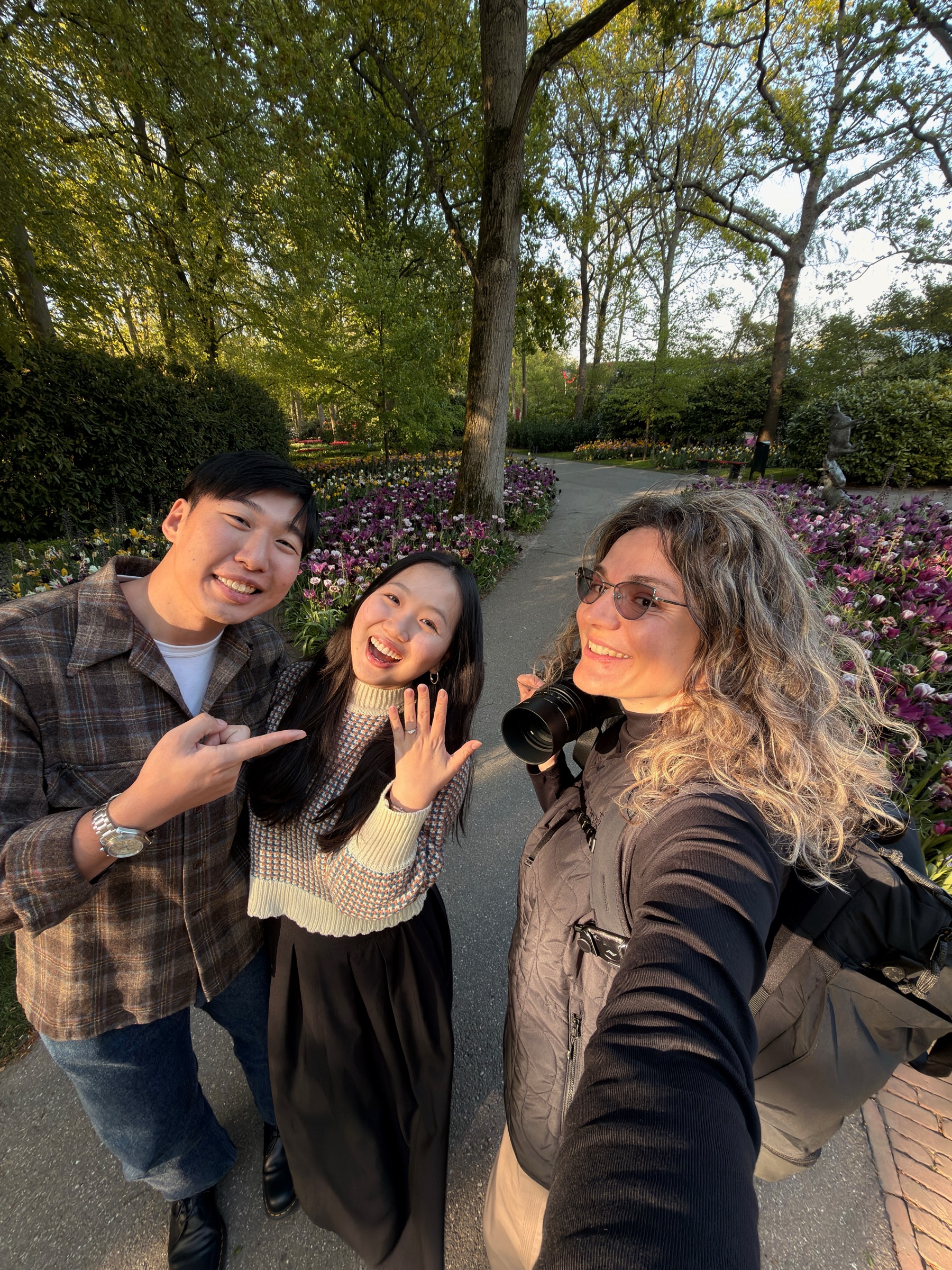 Selfie of the newly engaged couple and a woman holding a film camera, the young woman showing her ring on a garden path