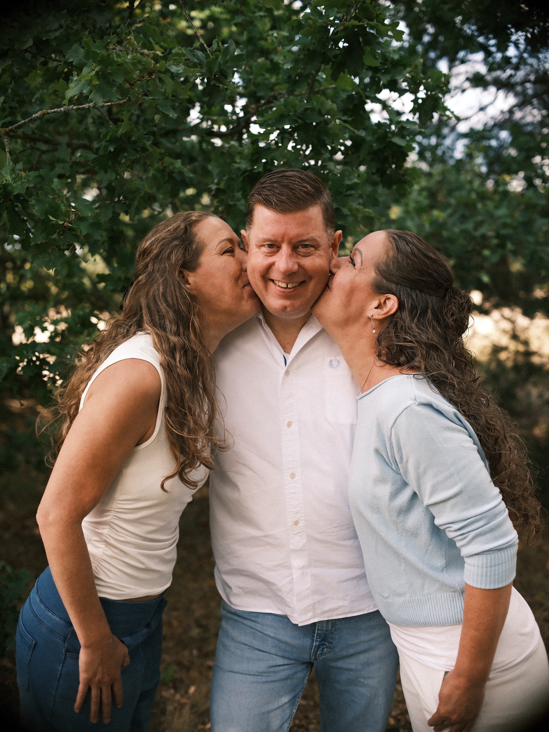 Two sisters kissing their brother on both cheeks at the same time, the three siblings framed by green oak leaves in the dunes