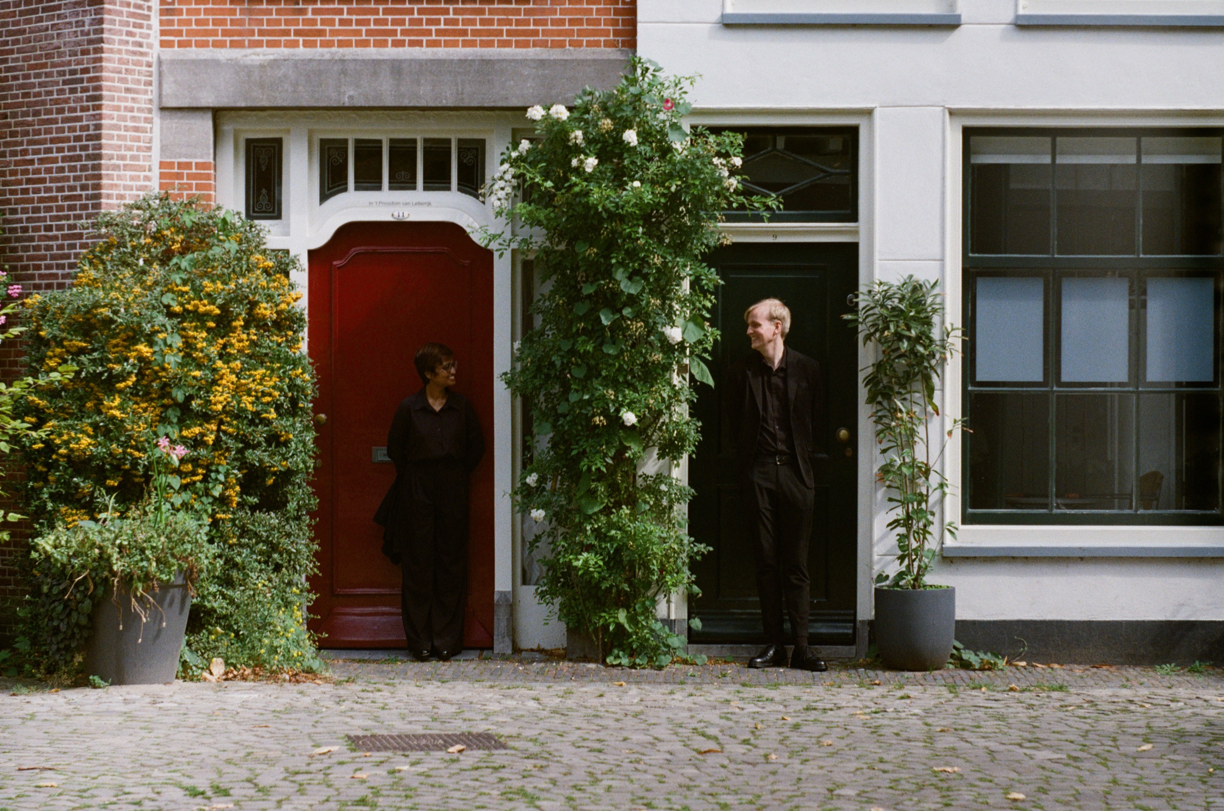 Small square in Leiden with a red door and a black door side by side, the couple in black in the two doorways and white roses between