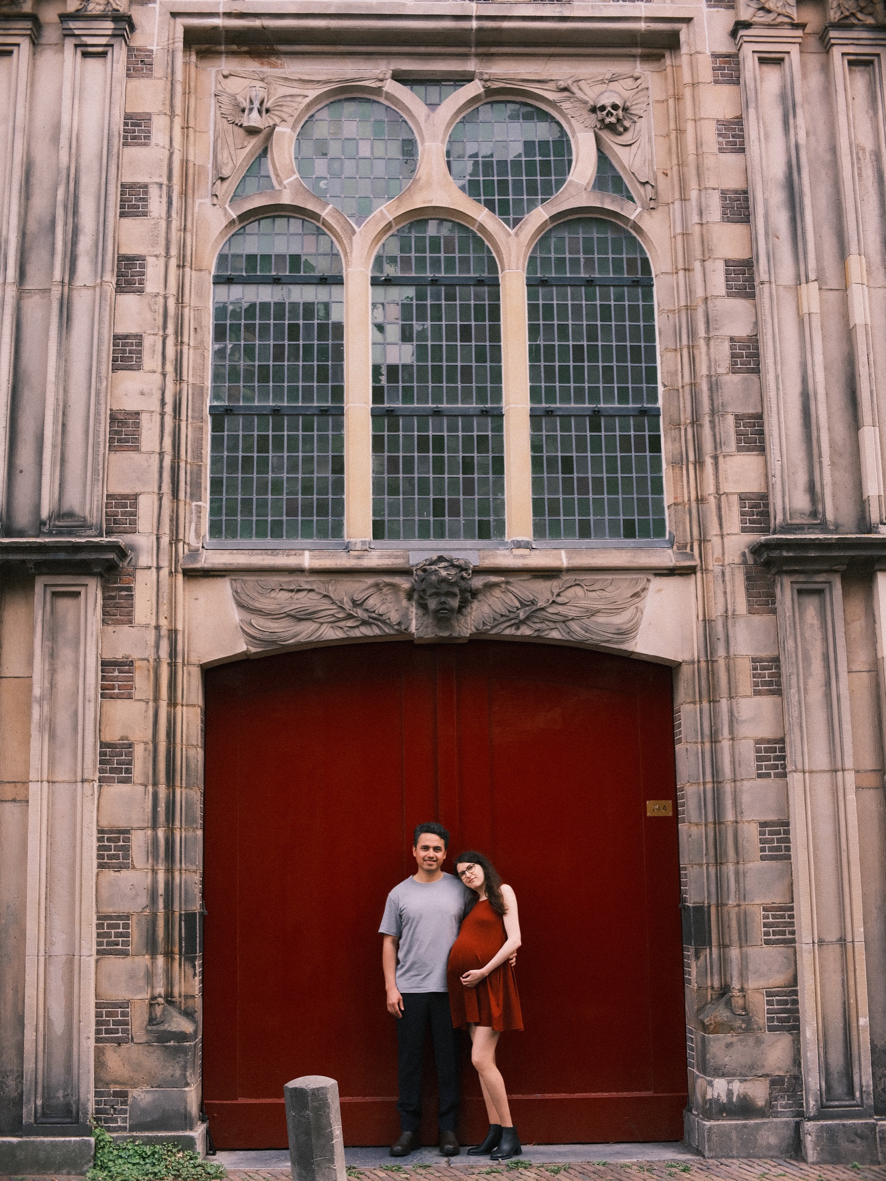 Stone facade with tall arched windows in Leiden and a red door below, the couple small and close together at its foot