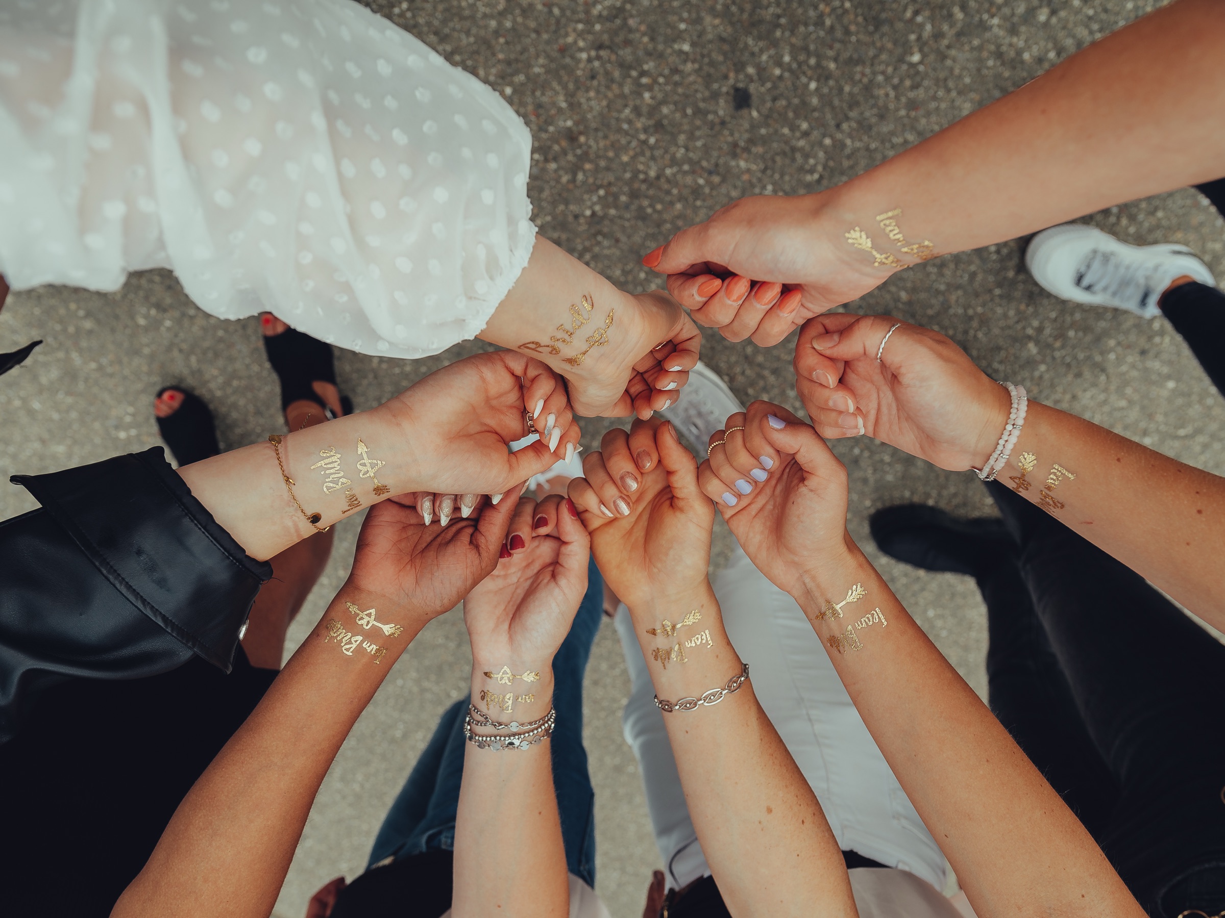 Wrists with gold Team Bride temporary tattoos meeting in a circle, seen from above, the bride's white polka-dot sleeve at the top