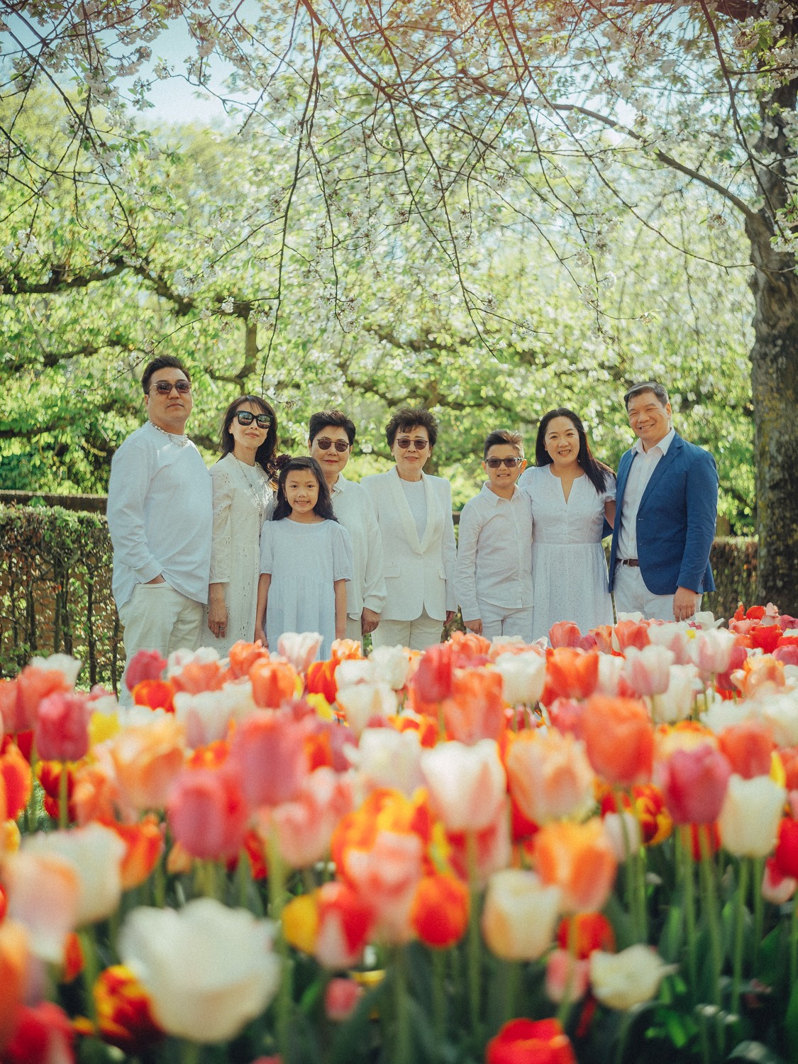 Drie generaties van één familie in het wit staan achter een perk met oranje, roze en witte tulpen in Keukenhof