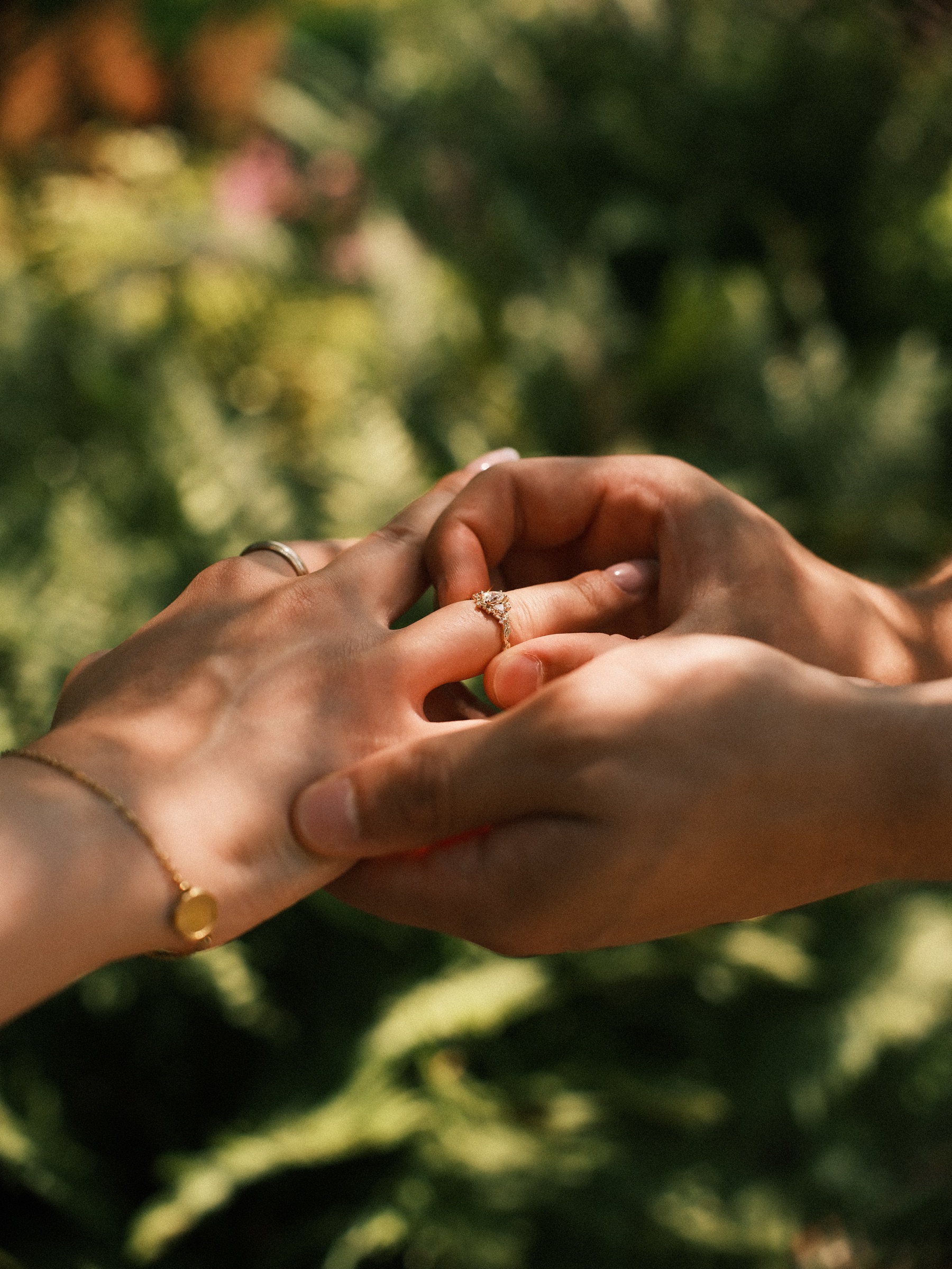 His fingers turning the ring on her hand in the shade, her gold bracelet with a round charm at the wrist, a detail of the proposal at Trompenburg