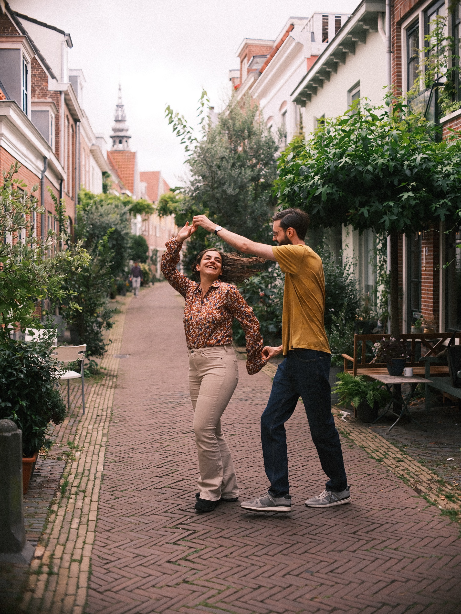 Man in een okergeel T-shirt laat zijn vriendin in een bloemetjesblouse ronddraaien in een smal Haarlems straatje vol zomerse planten