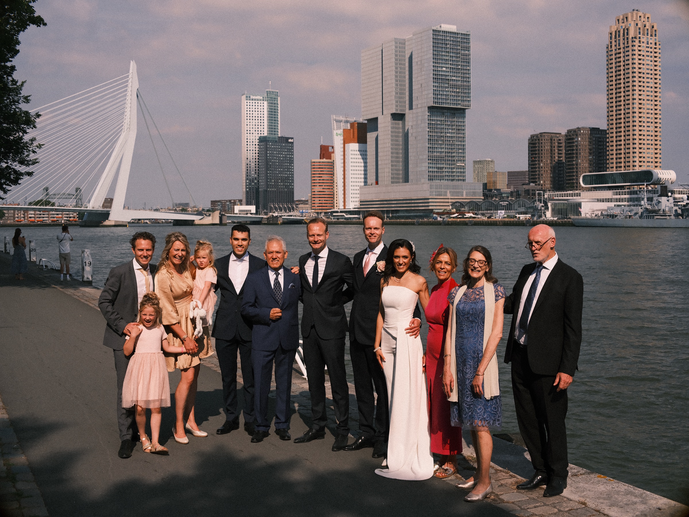 Twee families rond het bruidspaar op de kade langs de Maas, met de Erasmusbrug en de torens van de Kop van Zuid