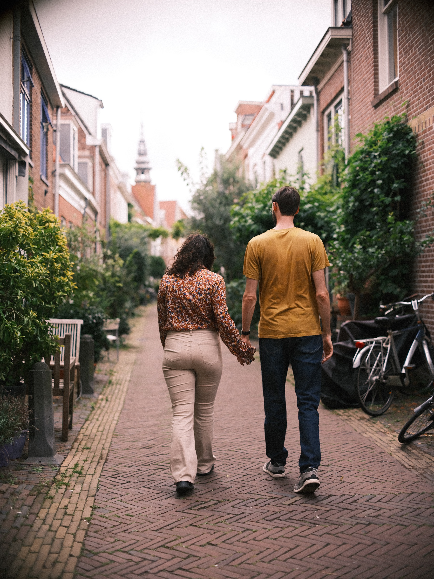 Stel loopt hand in hand weg door een smal groen straatje in Haarlem in de zomer, met een kerktoren aan het eind