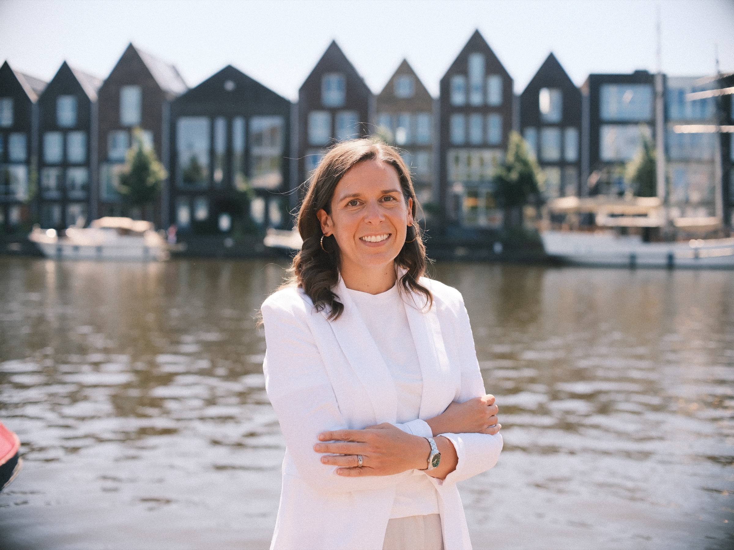 Lachende vrouw in witte blazer met de armen over elkaar aan het Spaarne, op een paar minuten lopen van molen De Adriaan