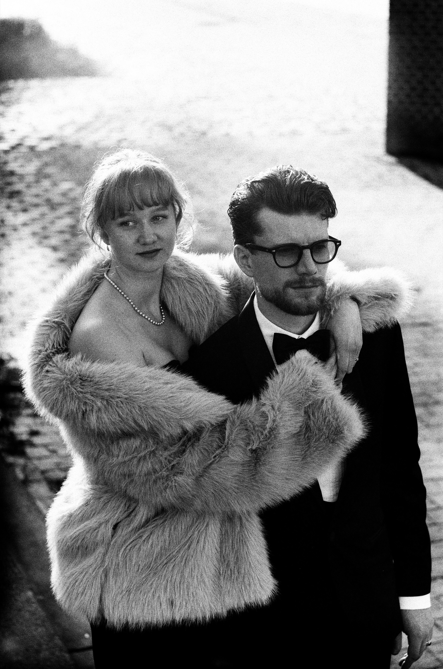 She wraps her arms and fur coat around his shoulders and looks into the lens, pearls at her neck, on black and white film in Rotterdam