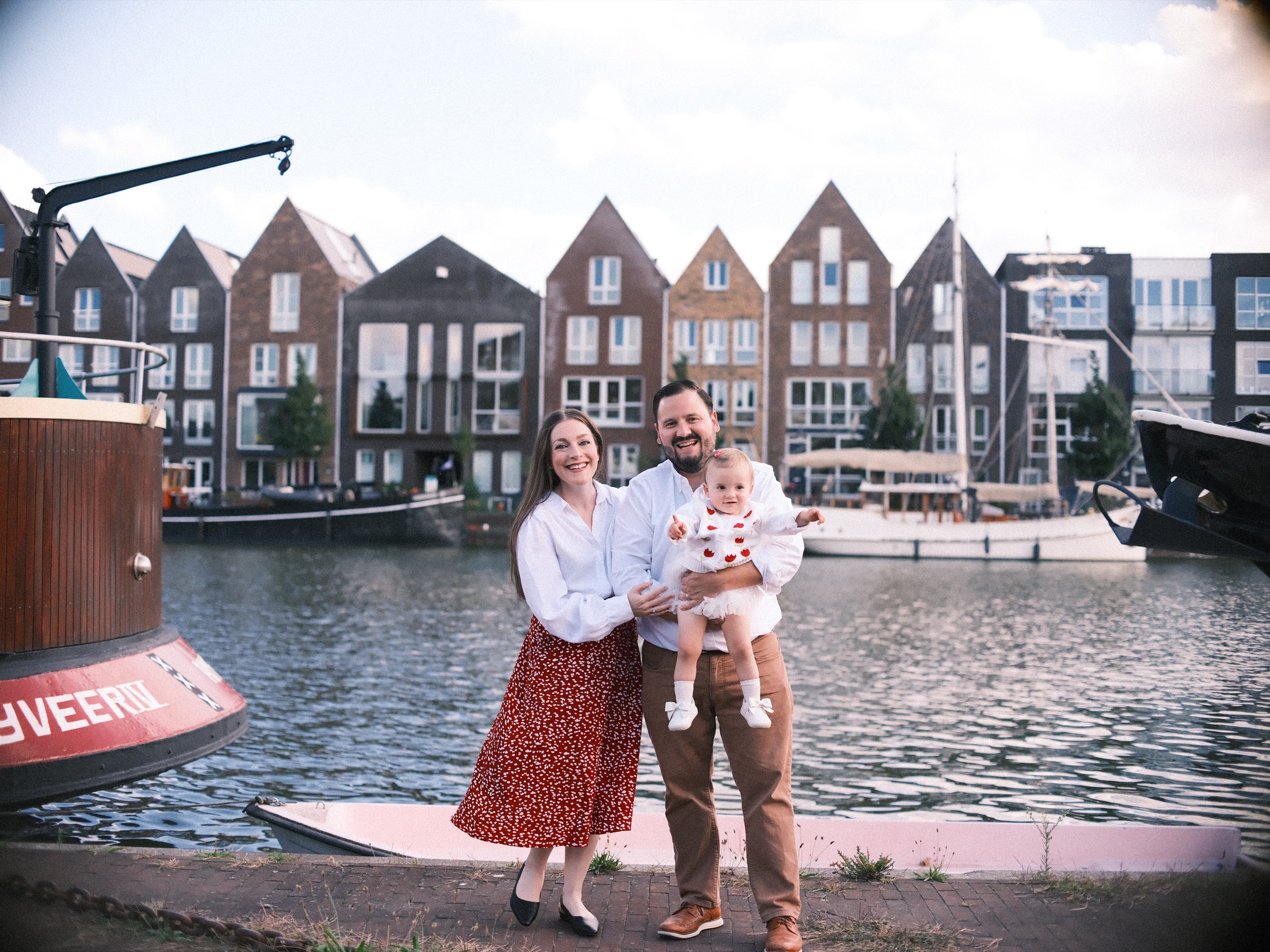 Ouders in witte overhemden met hun dochtertje aan het Spaarne, met een rij nieuwe huizen met puntgevels en boten aan de overkant